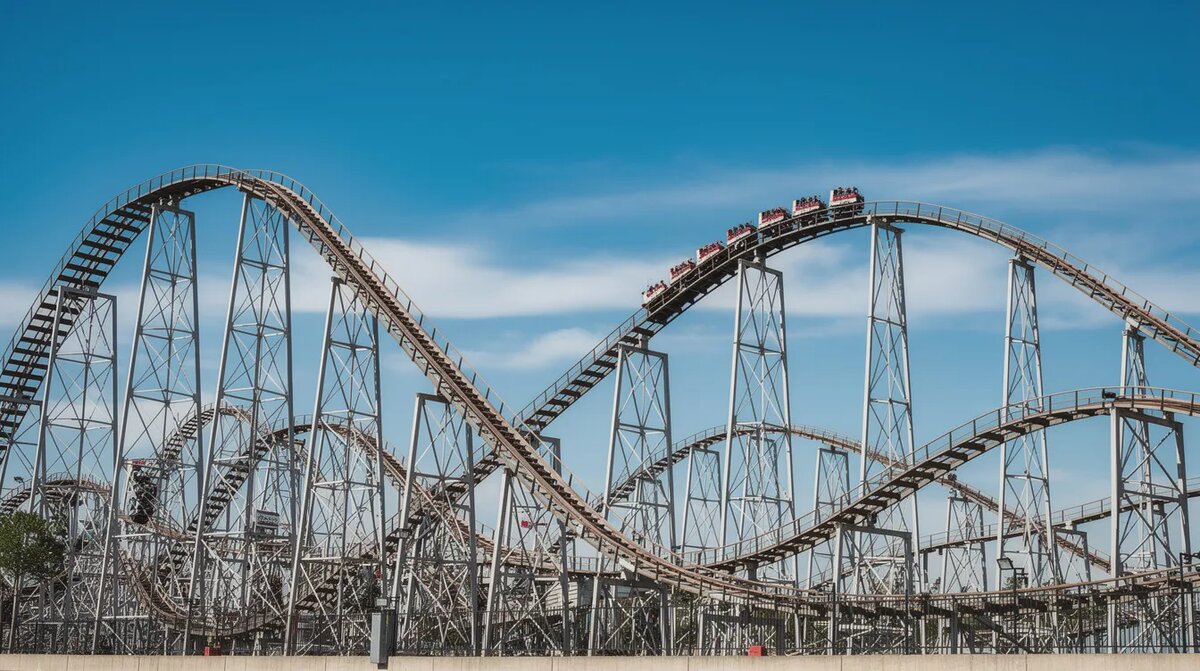 The image depicts a vibrant roller coaster soaring against a clear blue — Best Rtp